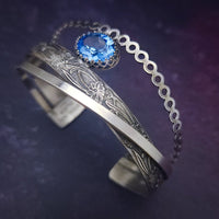 Made with three intricately intertwined sterling silver patterns, including a delicate bubble rope, intricate floral design, and sleek rectangle wire. Adorned with a shining 12x10 mm aquamarine gemstone in an open-backed silver filigree bezel, this bracelet sparkles and radiates a rainbow of colors with every movement.