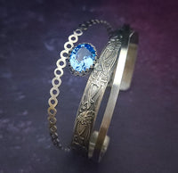 Made with three intricately intertwined sterling silver patterns, including a delicate bubble rope, intricate floral design, and sleek rectangle wire. Adorned with a shining 12x10 mm aquamarine gemstone in an open-backed silver filigree bezel, this bracelet sparkles and radiates a rainbow of colors with every movement.