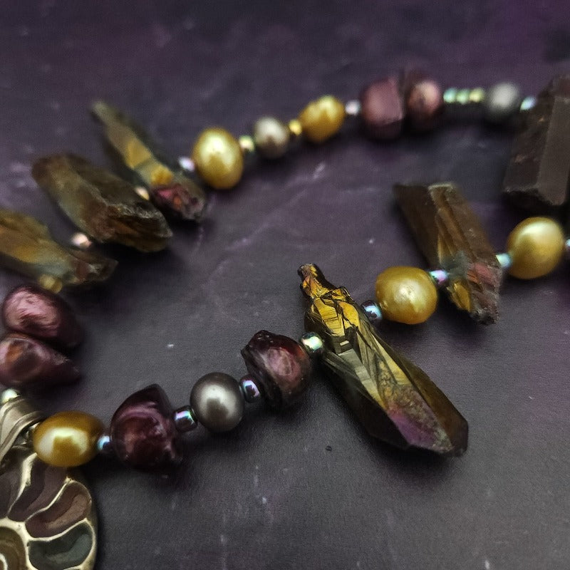 Make a bold statement with MARNIA, the one-of-a-kind necklace featuring titanium druzy, freshwater pearls, and a handcrafted bronze medallion ammonite. Turn heads with the vibrant colors and asymmetrical design, guaranteed to make you look and feel unforgettable!