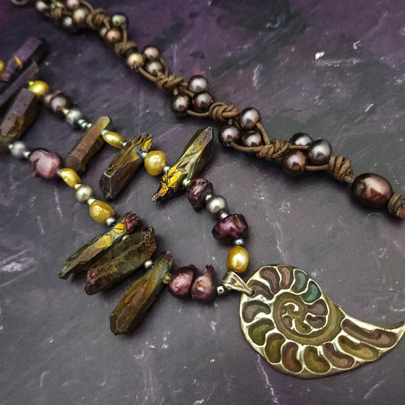 Make a bold statement with MARNIA, the one-of-a-kind necklace featuring titanium druzy, freshwater pearls, and a handcrafted bronze medallion ammonite. Turn heads with the vibrant colors and asymmetrical design, guaranteed to make you look and feel unforgettable!