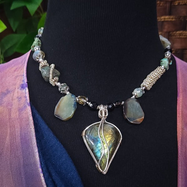 We all have a light within, an inner glow that others may see when they connect with our spirit. The shimmer and glow of this Labradorite Cabochon reminds me of this. This asymmetrical collar necklace is a testament to artisan craftsmanship and design. The Labradorite Cabochon is encased in a Wire Wrapped setting with a beautifully fluid look, and sterling silver coiled pieces add a unique look.