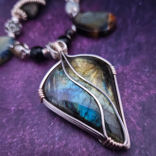 We all have a light within, an inner glow that others may see when they connect with our spirit. The shimmer and glow of this Labradorite Cabochon reminds me of this. This asymmetrical collar necklace is a testament to artisan craftsmanship and design. The Labradorite Cabochon is encased in a Wire Wrapped setting with a beautifully fluid look, and sterling silver coiled pieces add a unique look.