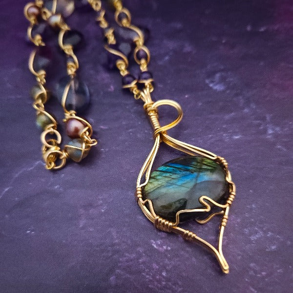 We all have a light within, an inner glow that others may see when they connect with our spirit. The shimmer and glow of this Labradorite Cabochon reminds me of this. This asymmetrical collar necklace is a testament to artisan craftsmanship and design. The Labradorite Cabochon is encased in a 14K Yellow Gold-Filled Wire Wrapped setting with a beautifully fluid look, and gold-wrapped pieces add a unique look.