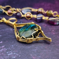 We all have a light within, an inner glow that others may see when they connect with our spirit. The shimmer and glow of this Labradorite Cabochon reminds me of this. This asymmetrical collar necklace is a testament to artisan craftsmanship and design. The Labradorite Cabochon is encased in a 14K Yellow Gold-Filled Wire Wrapped setting with a beautifully fluid look, and gold-wrapped pieces add a unique look.