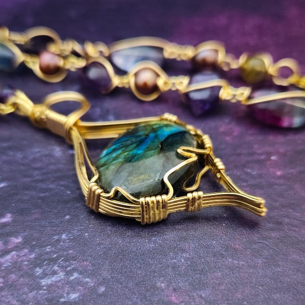 We all have a light within, an inner glow that others may see when they connect with our spirit. The shimmer and glow of this Labradorite Cabochon reminds me of this. This asymmetrical collar necklace is a testament to artisan craftsmanship and design. The Labradorite Cabochon is encased in a 14K Yellow Gold-Filled Wire Wrapped setting with a beautifully fluid look, and gold-wrapped pieces add a unique look.