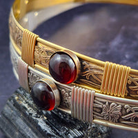 Gold bracelet with red gemstones on a textured surface