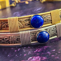 Two ornate bracelets with blue stones on a purple surface