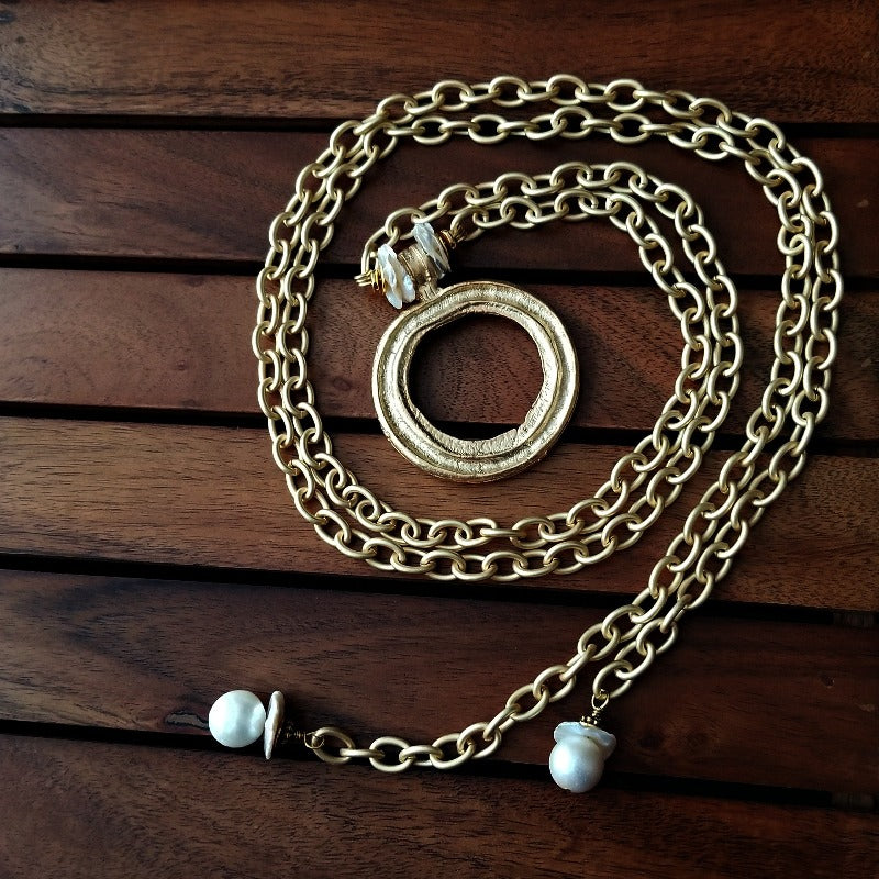 THE 5th AVENUE LARIAT is bold and dramatic, and will definitely get some attention. A large circular disc attached to gold Brittanium chain with both wafer and large freshwater pearls. Simply place the circle where you want it, wrap the chain around your neck and slide the ends thru the circle. Voila! Instant Fashionista!