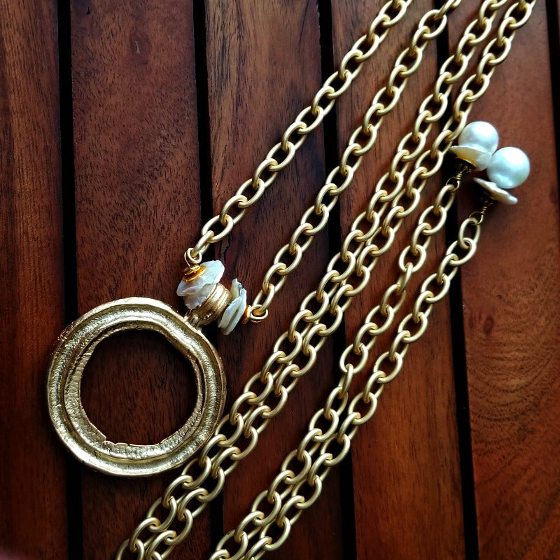 THE 5th AVENUE LARIAT is bold and dramatic, and will definitely get some attention. A large circular disc attached to gold Brittanium chain with both wafer and large freshwater pearls. Simply place the circle where you want it, wrap the chain around your neck and slide the ends thru the circle. Voila! Instant Fashionista!