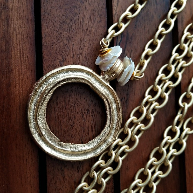 THE 5th AVENUE LARIAT is bold and dramatic, and will definitely get some attention. A large circular disc attached to gold Brittanium chain with both wafer and large freshwater pearls. Simply place the circle where you want it, wrap the chain around your neck and slide the ends thru the circle. Voila! Instant Fashionista!