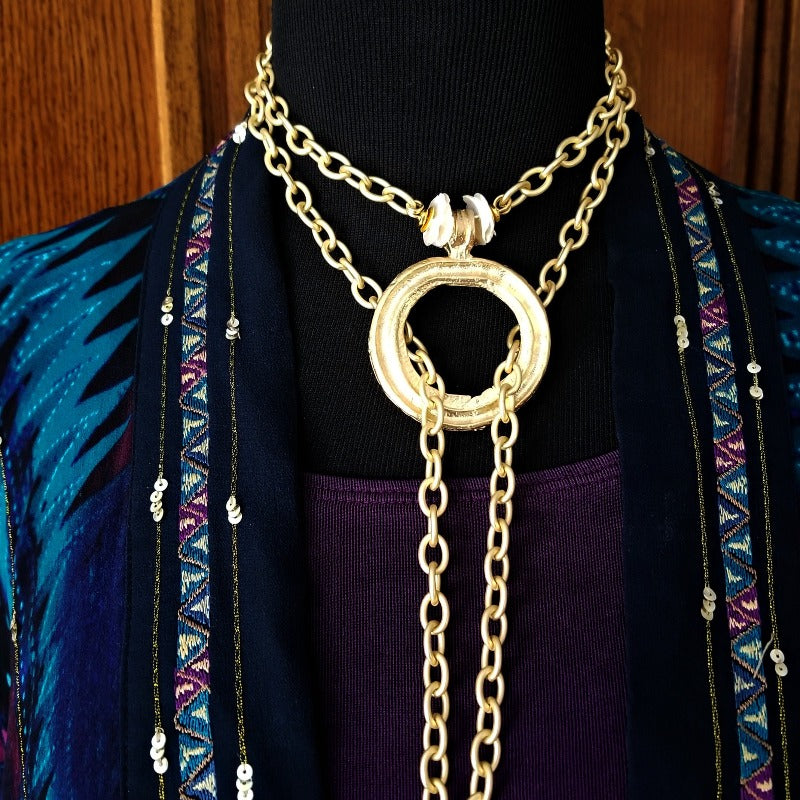 THE 5th AVENUE LARIAT is bold and dramatic, and will definitely get some attention. A large circular disc attached to gold Brittanium chain with both wafer and large freshwater pearls. Simply place the circle where you want it, wrap the chain around your neck and slide the ends thru the circle. Voila! Instant Fashionista!