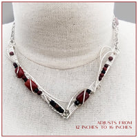 This collar is hand crafted and wrapped with strands of luscious sterling silver wire and embellished with Red Jasper and Black Onyx. Gemstones and accent beads are incorporated securely into the wire work. Flowing curves soften the hard lines of the metals and an asymmetrical flair makes this an unusual and dramatic addition to your private collection.