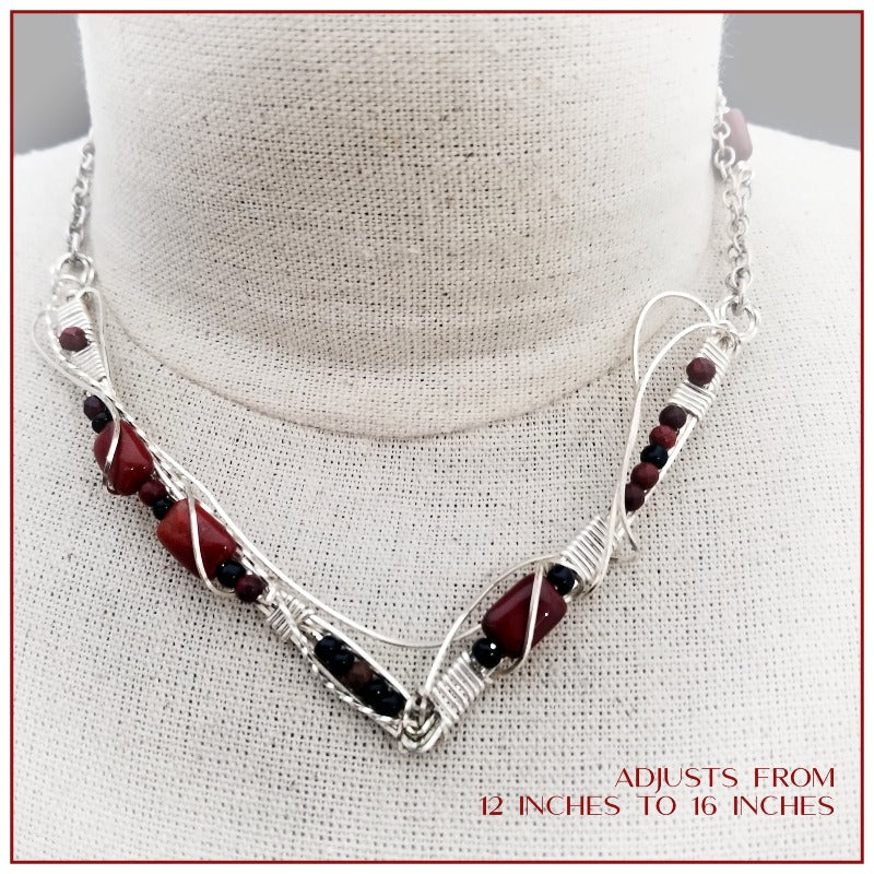 This collar is hand crafted and wrapped with strands of luscious sterling silver wire and embellished with Red Jasper and Black Onyx. Gemstones and accent beads are incorporated securely into the wire work. Flowing curves soften the hard lines of the metals and an asymmetrical flair makes this an unusual and dramatic addition to your private collection.
