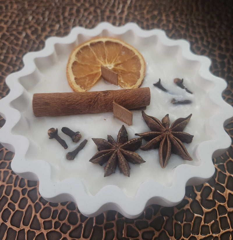 Concrete Bowl Candle with spices including cinnamon sticks, star anise, and cloves on a decorative white plate with a textured brown background.