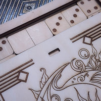 Close-up of a wooden game board with engraved geometric and floral designs, light natural wood domino tiles, and a blue patterned section in the upper left.