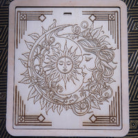 A square wooden decorative plaque or board featuring a laser-engraved sun and moon design with a woman's face, surrounded by leaves and ornate corner patterns, shown on a dark patterned fabric background.