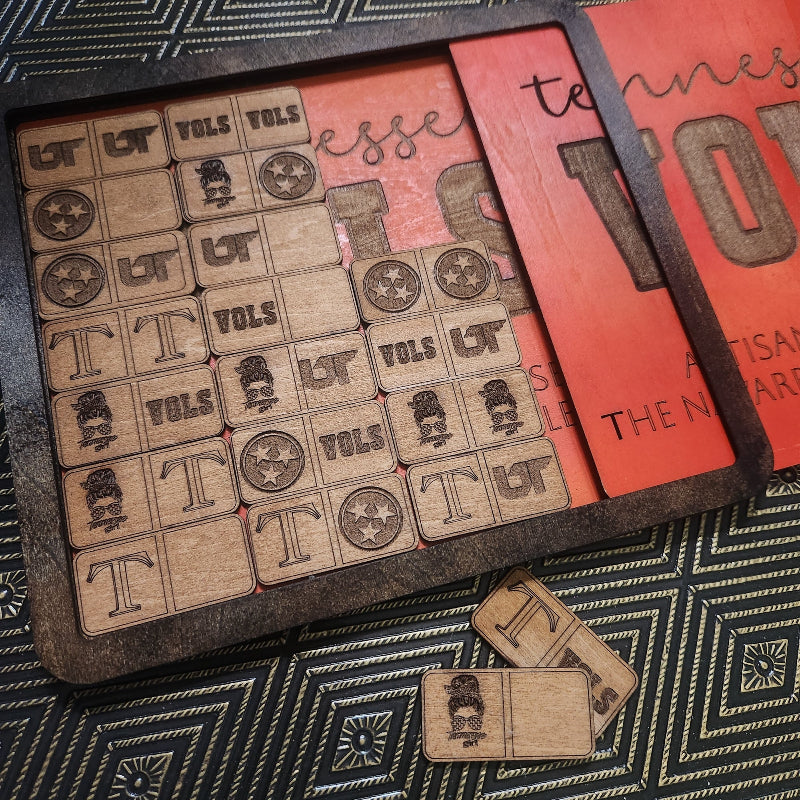 A wooden game board set with engraved wooden tokens featuring letters and stars, displayed on a dark patterned surface next to a red decorative card.