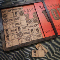 A wooden game board set with engraved wooden tokens featuring letters and stars, displayed on a dark patterned surface next to a red decorative card.