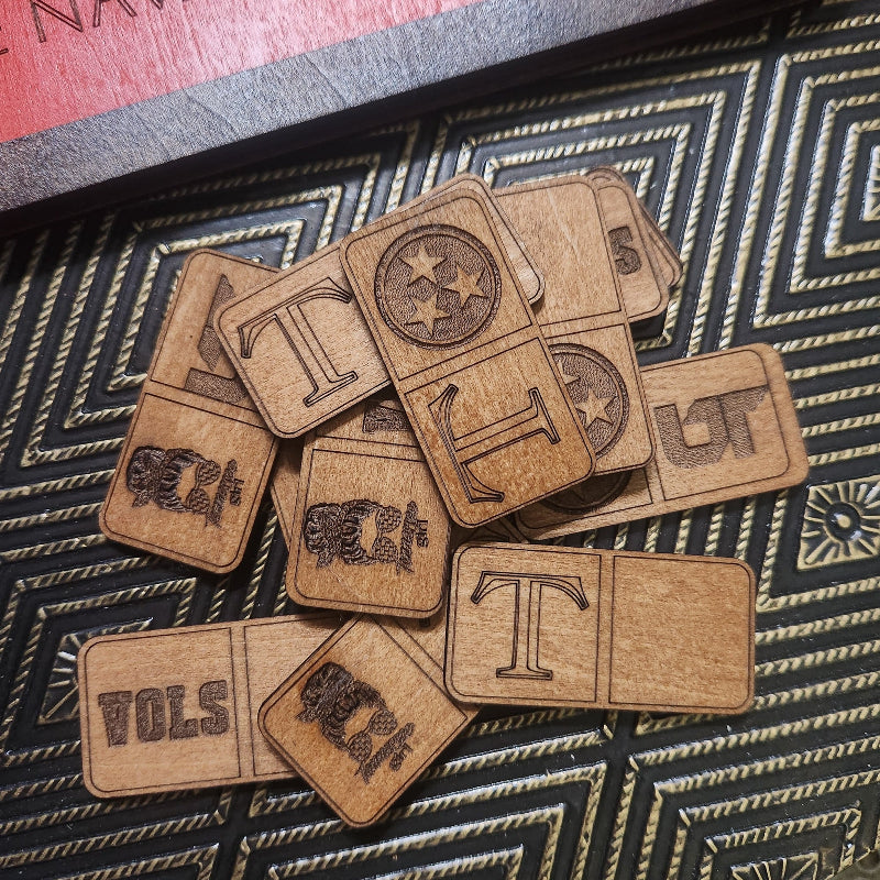 A pile of wooden letter tiles with engraved letters and symbols, arranged on a black and gold patterned surface.