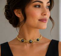 Woman wearing a gold necklace with black stones against a neutral background