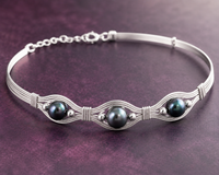 Silver bracelet with three dark pearls on a purple background