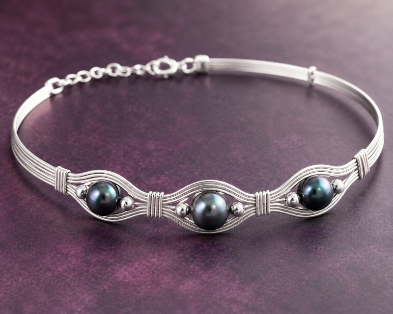 Silver bracelet with three dark pearls on a purple background