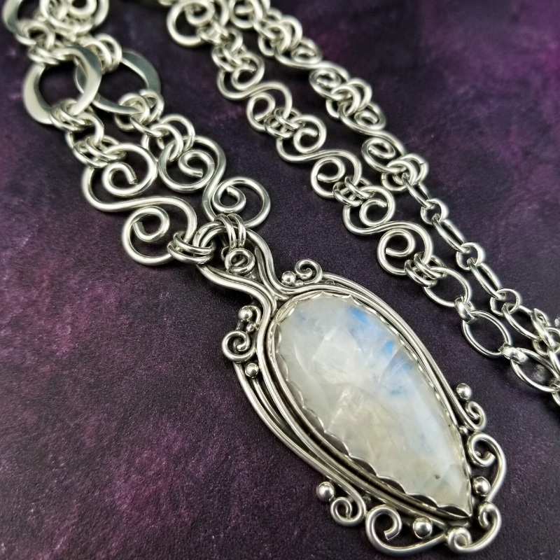 Silver chain necklace with a central gemstone pendant on a purple textured background