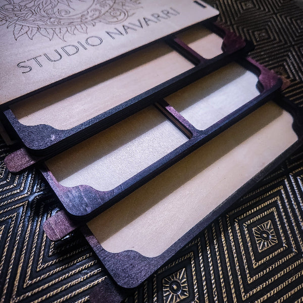 A close-up of a wooden multi-compartment organizer tray with dark stained edges and light natural wood interiors, shown on a patterned black and gold surface. A branded lid or insert reading STUDIO NAVARRI is visible at the top.