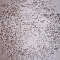 A close-up of a light beige wood with an intricate engraved line-art design featuring a sun face, moon face, flowing hair, and leafy ornamental swirls.