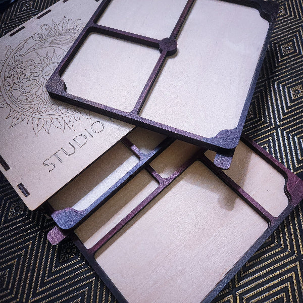 Laser-cut wooden organizer trays and a matching storage box with a decorative sunburst engraving and the word 'STUDIO' on a patterned black and gold fabric background.