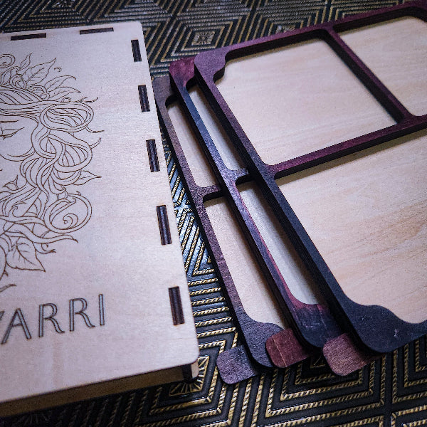 Laser-cut wooden jewelry box components and inner trays, including a lid engraved with floral detailing and the word 'YARRI', shown on a patterned dark surface.