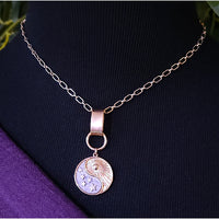 A rose gold chain necklace with a pendant featuring a yin-yang symbol and a sun, displayed on a black mannequin bust with a purple fabric accent.