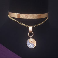 A gold-toned double-layer necklace displayed on a black mannequin bust, featuring a wide mesh-style top band and a delicate chain with a round pendant. The pendant has a yin-yang design with one half in gold and the other in a pale blue-gray, accented with small white stars.