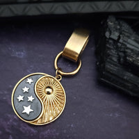 A gold and silver-toned yin-yang keychain charm with stars on a dark purple textured background next to a black crystal.