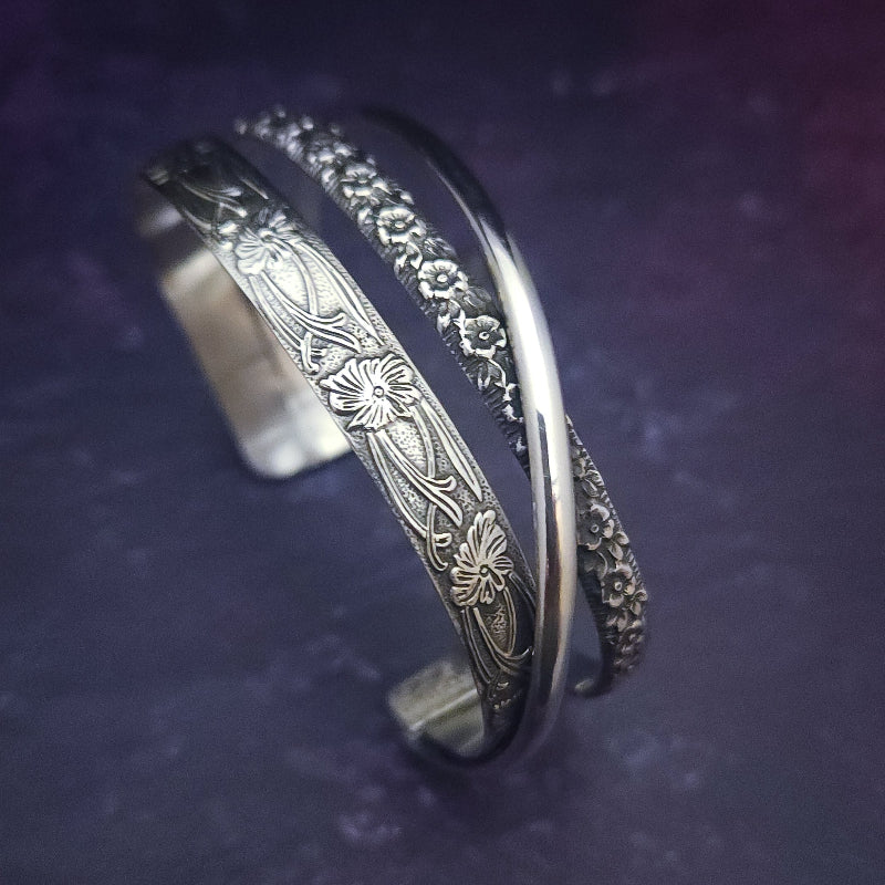 Discover the elegance of our CROSSOVER Cuff No. 4 with its trio of intricate sterling silver patterns that seamlessly intertwine to create a one-of-a-kind bracelet. Pair it with our collars for the ultimate statement piece. The Soft and Sweet and Lokelani Rose patterns are beautifully crafted with a polished sterling wire.