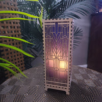 Domara LED lamp with Frank Lloyd Wright inspired Arts and Craftsman styled lamp on a dark surface next to a plant
