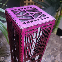 Pink geometric-patterned box on a textured surface with plants in the background