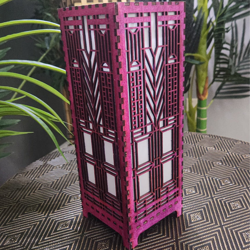 Pink decorative lamp with geometric patterns on a patterned surface with plants in the background