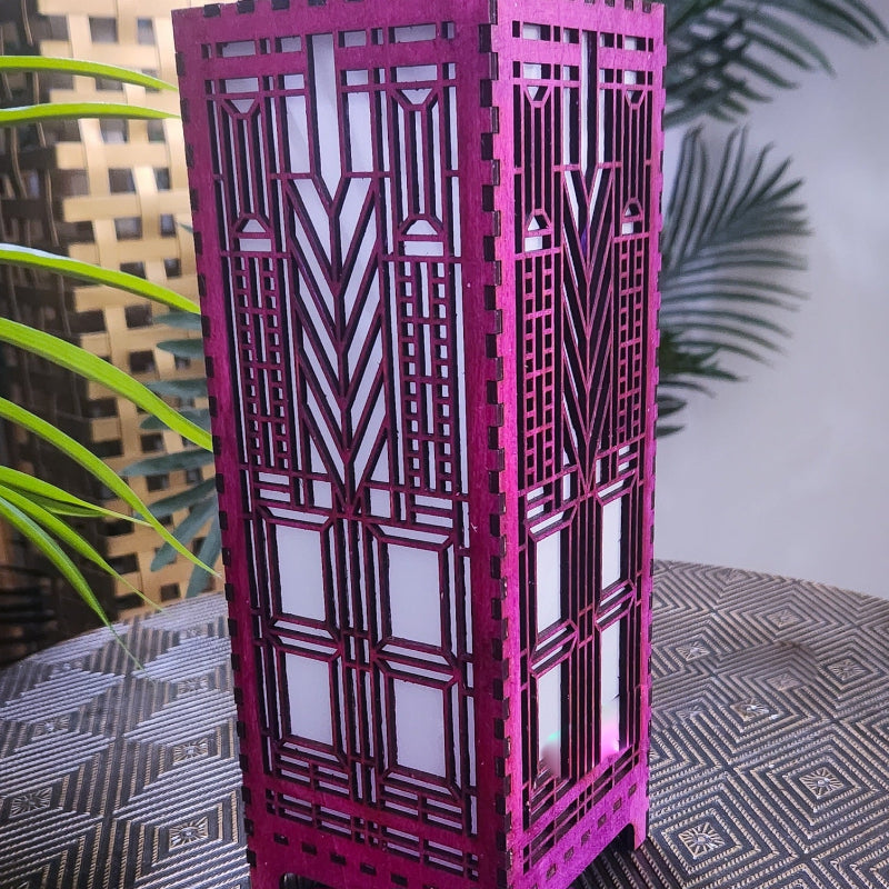 Purple decorative lantern with geometric patterns on a textured surface with plants in the background