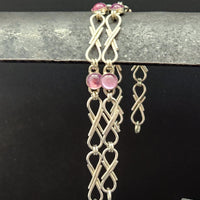 A sterling ribbon link bracelet with pink round gemstone accents, displayed against a black background with a textured gray bar at the top.