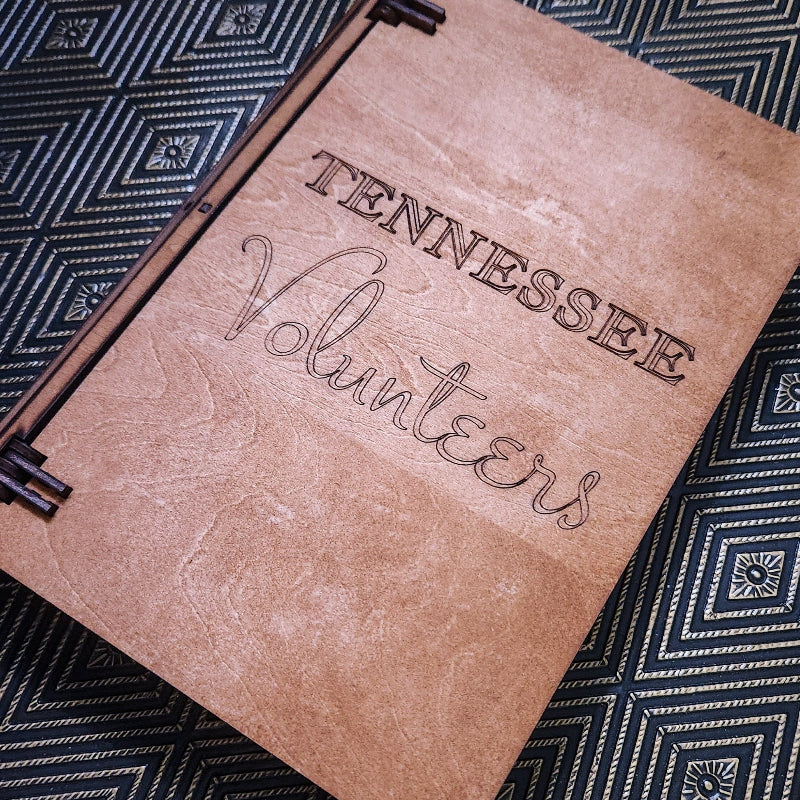 A brown faux-leather binder or notebook cover with 'TENNESSEE Volunteers' engraved on the front, shown closed on a black and white geometric patterned surface.