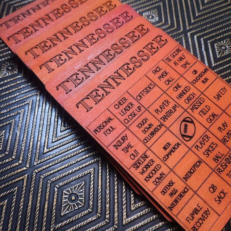 A close-up of a wooden Tennessee football-themed card or game board with engraved text and a football icon, placed diagonally on a dark patterned surface.