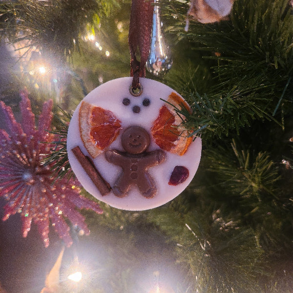 Decorative ornament with gingerbread man, cinnamon stick, and orange slices on a Christmas tree.