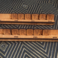 Two wooden letter tiles on matching wooden racks, arranged to spell out words on a dark patterned fabric background.