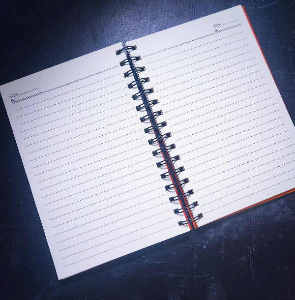 An open spiral-bound lined notebook with blank pages, photographed at an angle on a dark textured surface.