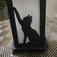 Black silhouette of a cat on a white candle inside a decorative holder with a geometric patterned surface.