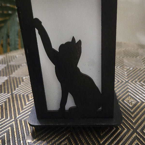 Black silhouette of a cat on a white candle inside a decorative holder with a geometric patterned surface.