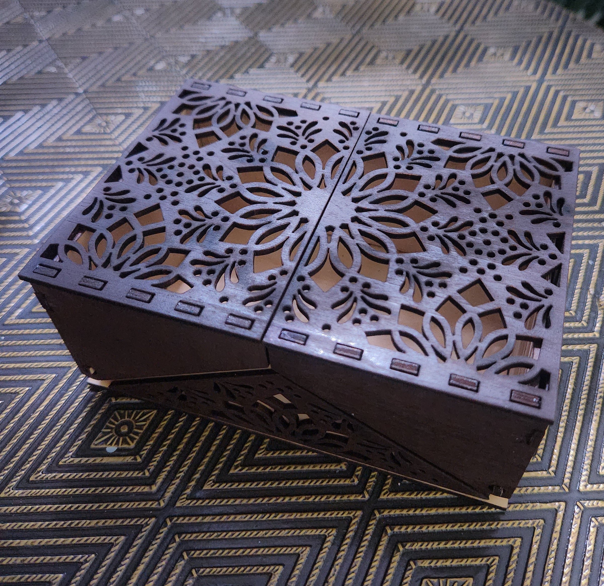 Decorative wooden box with intricate cut-out design on a patterned surface
