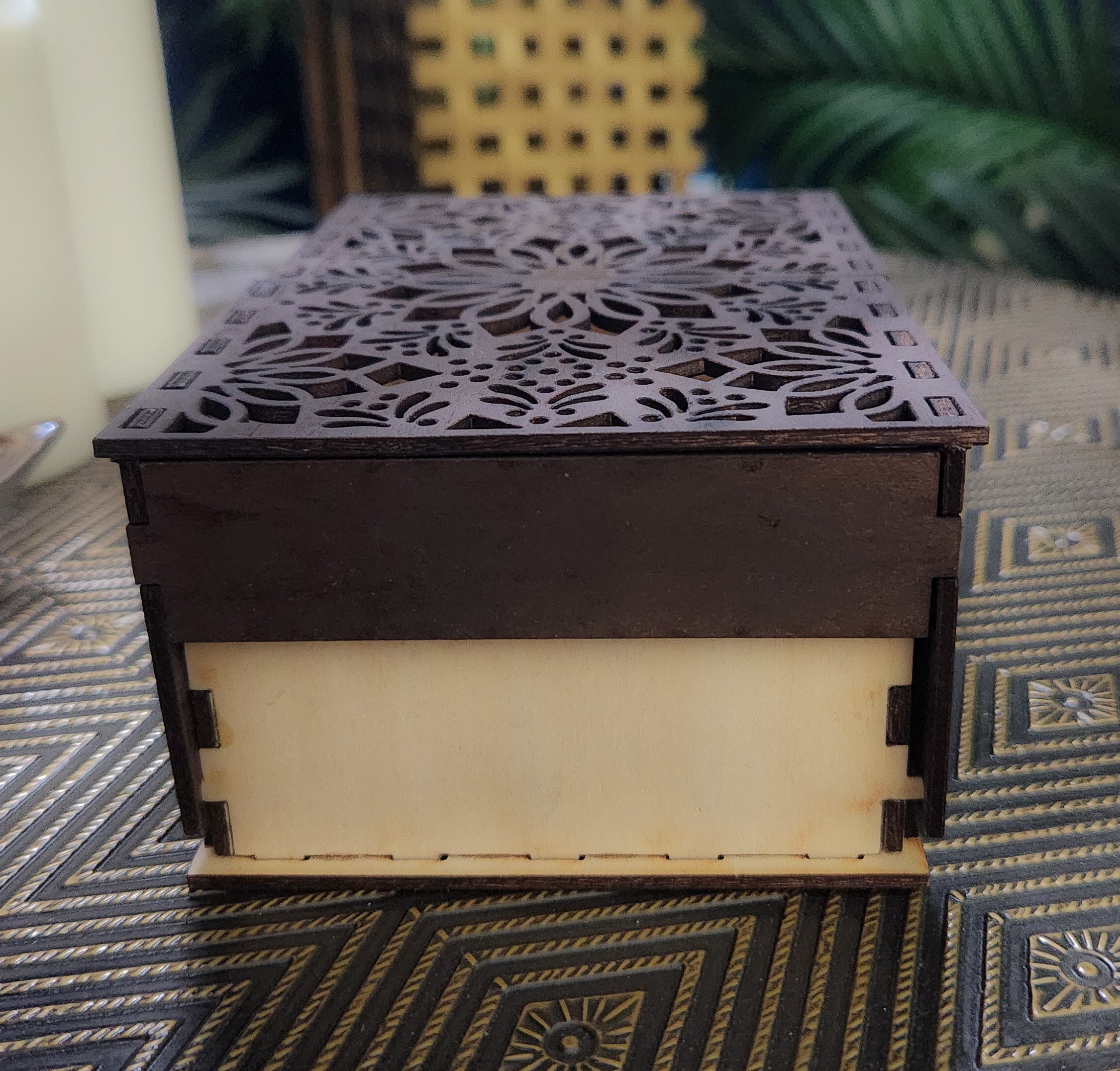 Wooden box with intricate laser-cut design on top, placed on a patterned surface.