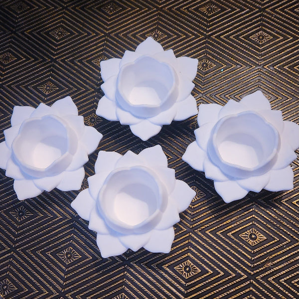 Four white lotus-shaped candles on a patterned surface